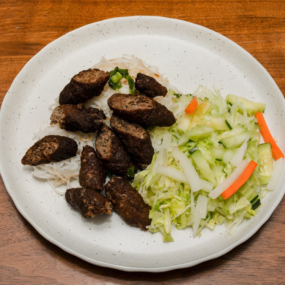 Ooh Pho's Vietnamese dish with dark brown sausage pieces, rice noodles, and a fresh salad.